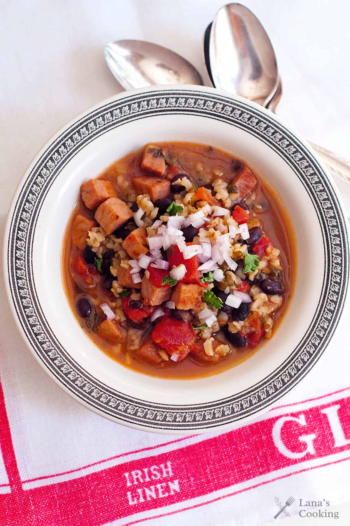 A bowl of soup with beans, diced meat, and rice, garnished with raw onion and herbs.