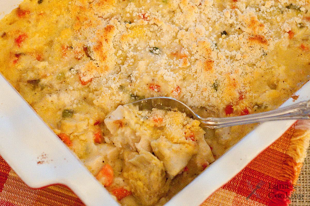 A spoon scoops cheesy, baked casserole topped with breadcrumbs in a white dish.