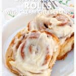 Two cinnamon rolls topped with cream cheese icing on a plate, with a fork beside them.