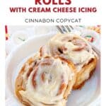 Two cinnamon rolls with cream cheese icing on a white plate, fork on the side, bright background.