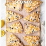 Seven lemon blueberry scones with icing on parchment paper, surrounded by lemon halves and a beige towel.