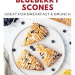 Three lemon blueberry scones with icing and blueberries on a white plate, viewed from above.