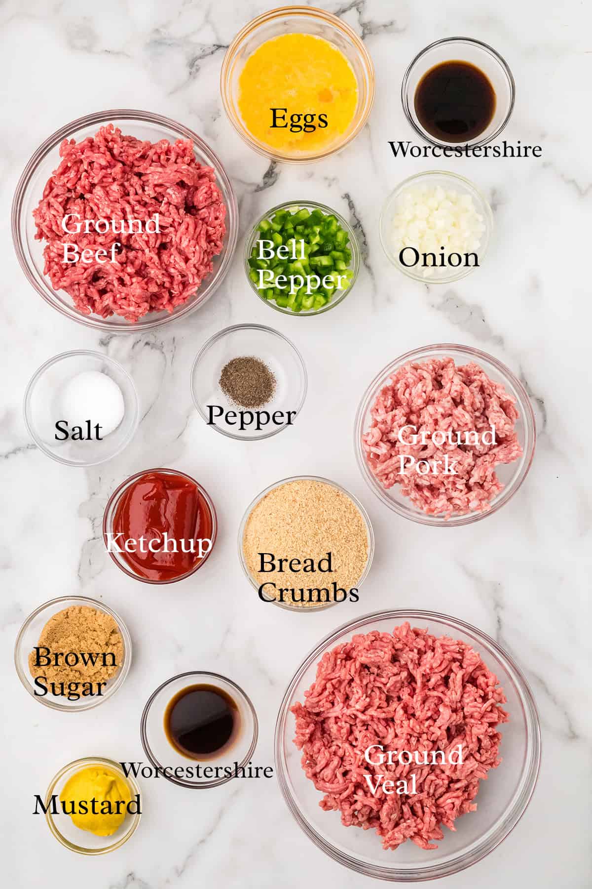 Bowls of ground beef, pork, veal, and ingredients for meatloaf including seasonings, eggs, and vegetables.
