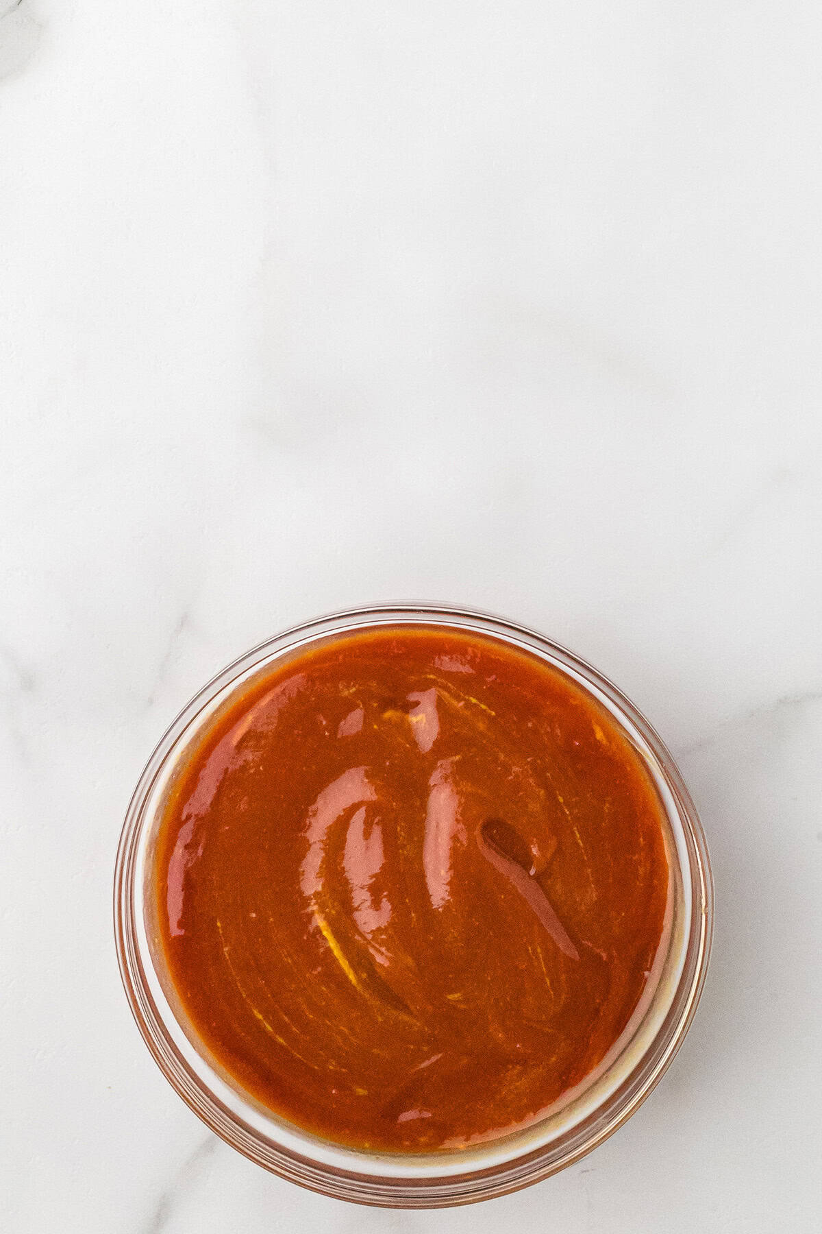 A small glass bowl filled with sauce on a white marble surface.