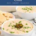 Two bowls of creamy white chicken chili topped with parsley and a jalapeño slice, served with bread.