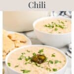 Two bowls of white chicken chili topped with cilantro and a jalapeño slice, with side pieces of bread.