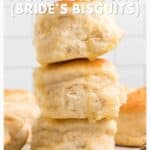 Three golden, fluffy biscuits stacked on each other, with more biscuits in the background on a light surface.