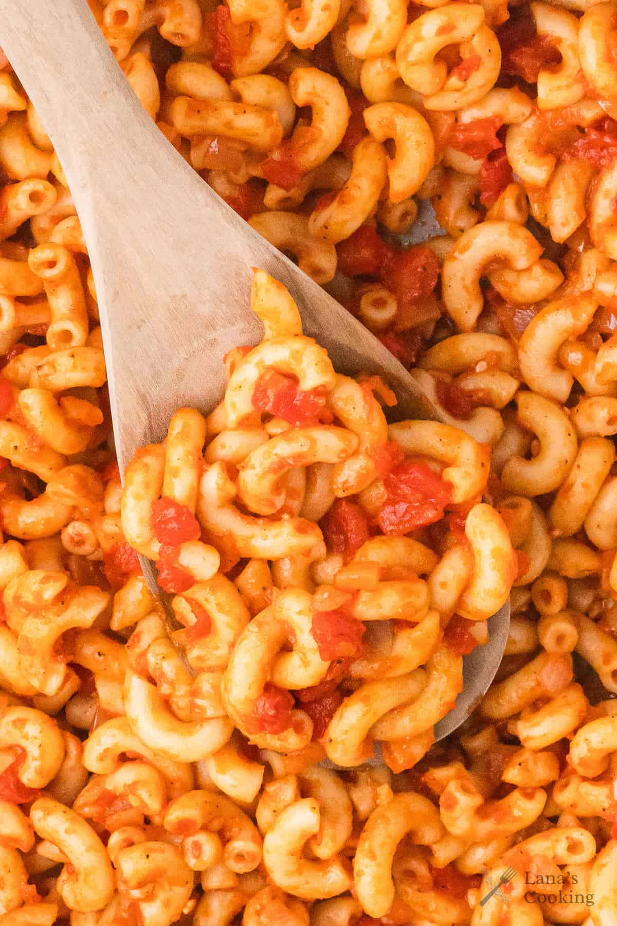 A wooden spoon scooping macaroni pasta in tomato sauce with diced tomatoes.