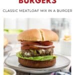 A meatloaf burger with lettuce, onions, and tomato on a plate, with fries and a drink in the background.