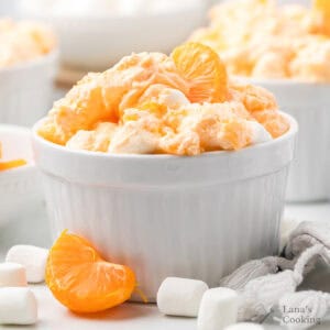 A white bowl filled with orange fluff salad, topped with mandarin slices and surrounded by marshmallows.