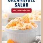 A white bowl of orange creamsicle salad with mandarin slices and mini marshmallows, on a white surface.