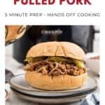 Pulled pork sandwich with pickles on a plate, slow cooker in background, recipe text above.