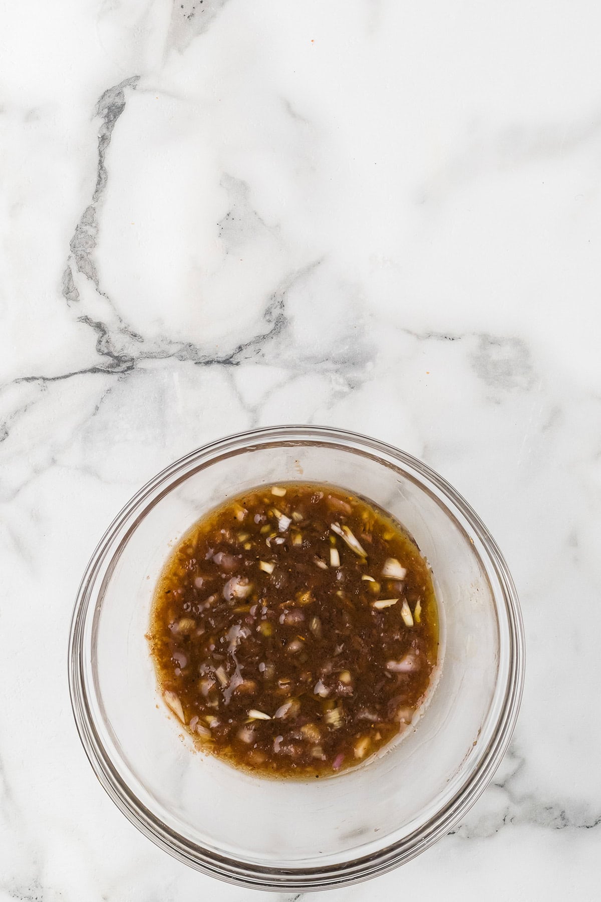 A glass bowl filled with a basamic dressing on a white marble surface.