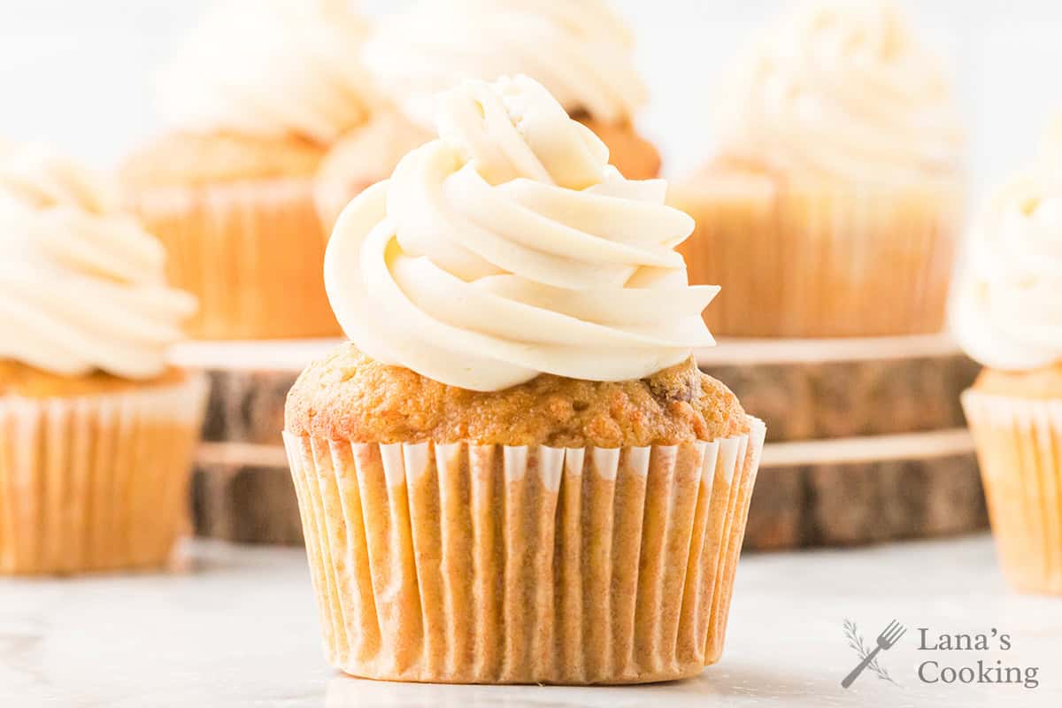 A cupcake with swirled frosting, surrounded by more cupcakes on a light background.