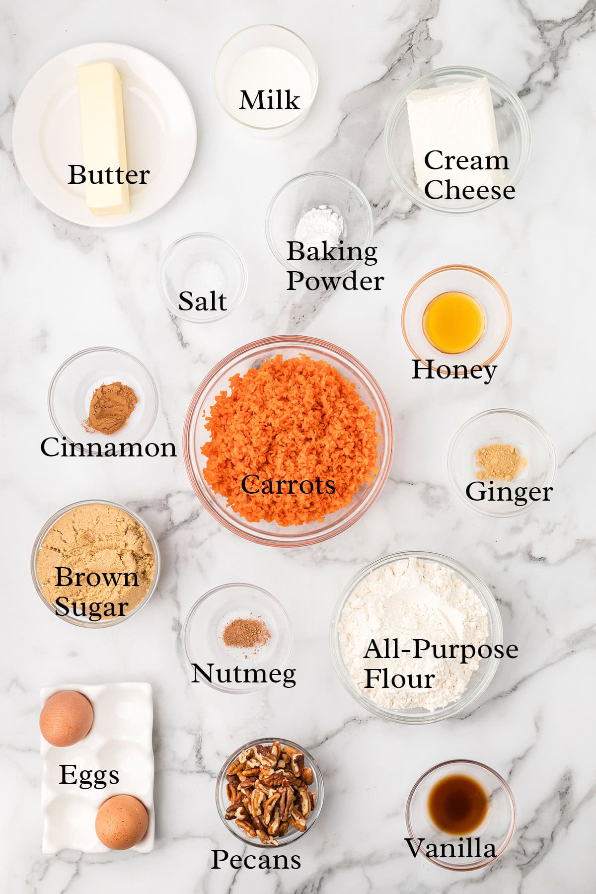 Ingredients for carrot cake, including carrots, flour, eggs, butter, spices, brown sugar, and pecans, on a marble surface.