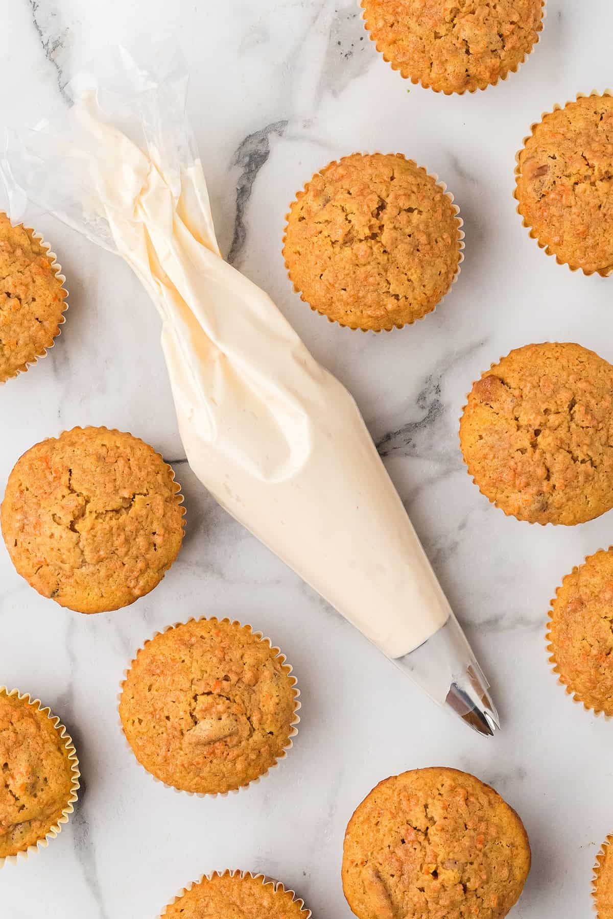 Cupcakes arranged around a piping bag filled with frosting on a white marble surface.