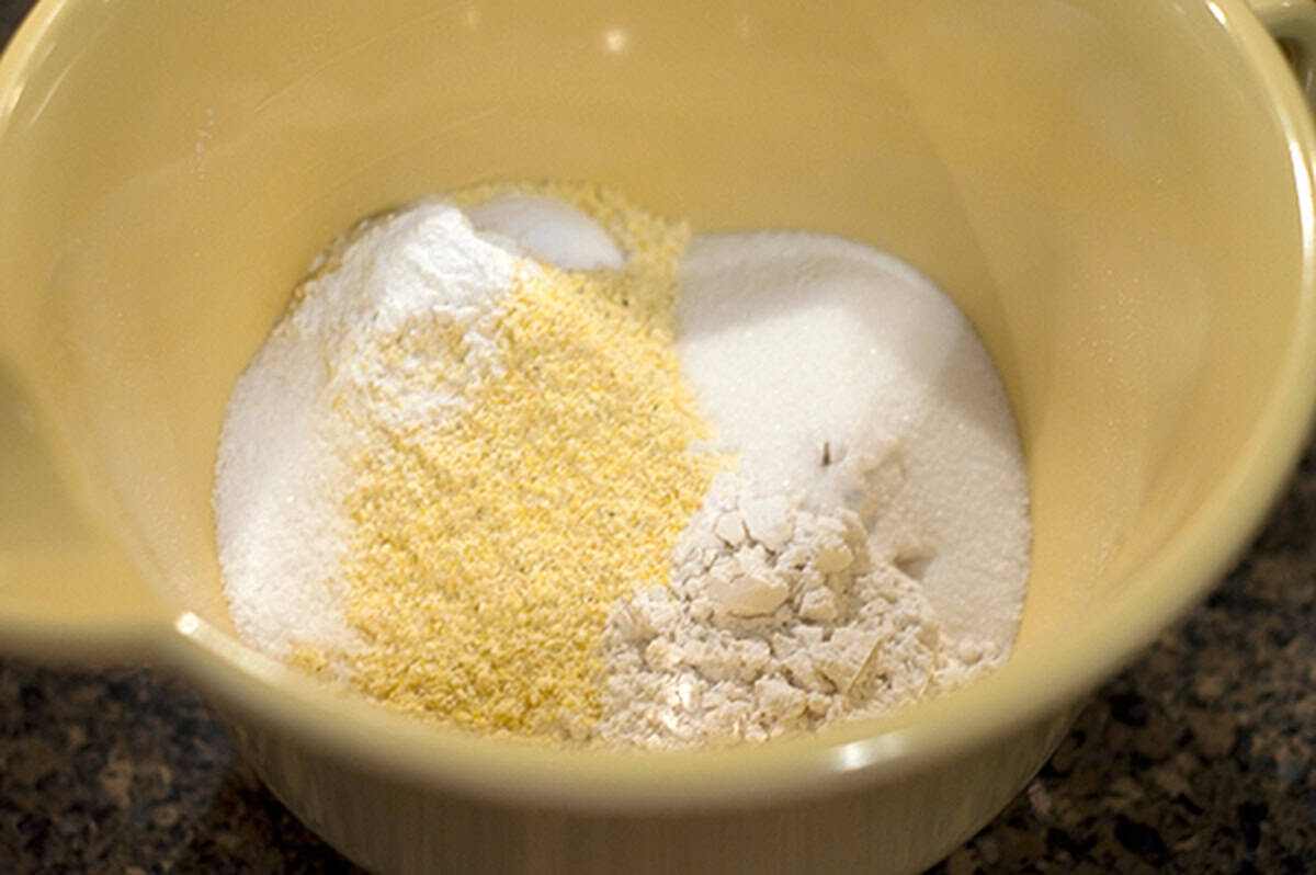 A mixing bowl with cornmeal, flour, sugar, and baking powder separated inside.