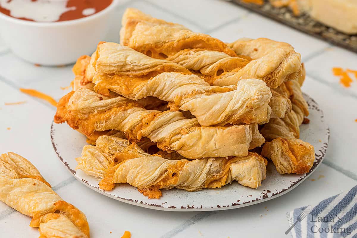 A plate stacked with golden, crispy cheese puff pastry twists on a light table.