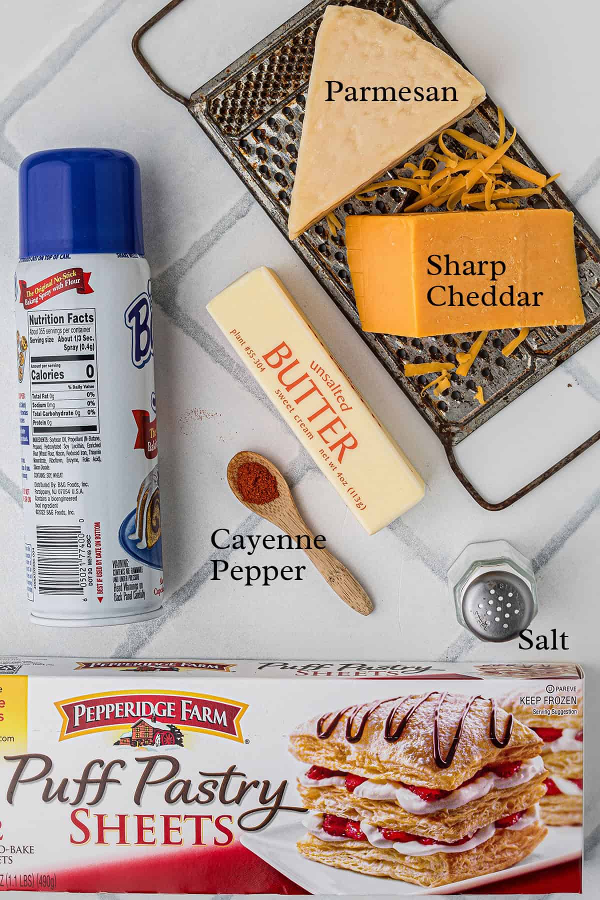 Labeled ingredients for cheese straws: Parmesan, sharp cheddar, butter, salt, cayenne pepper, puff pastry, spray.