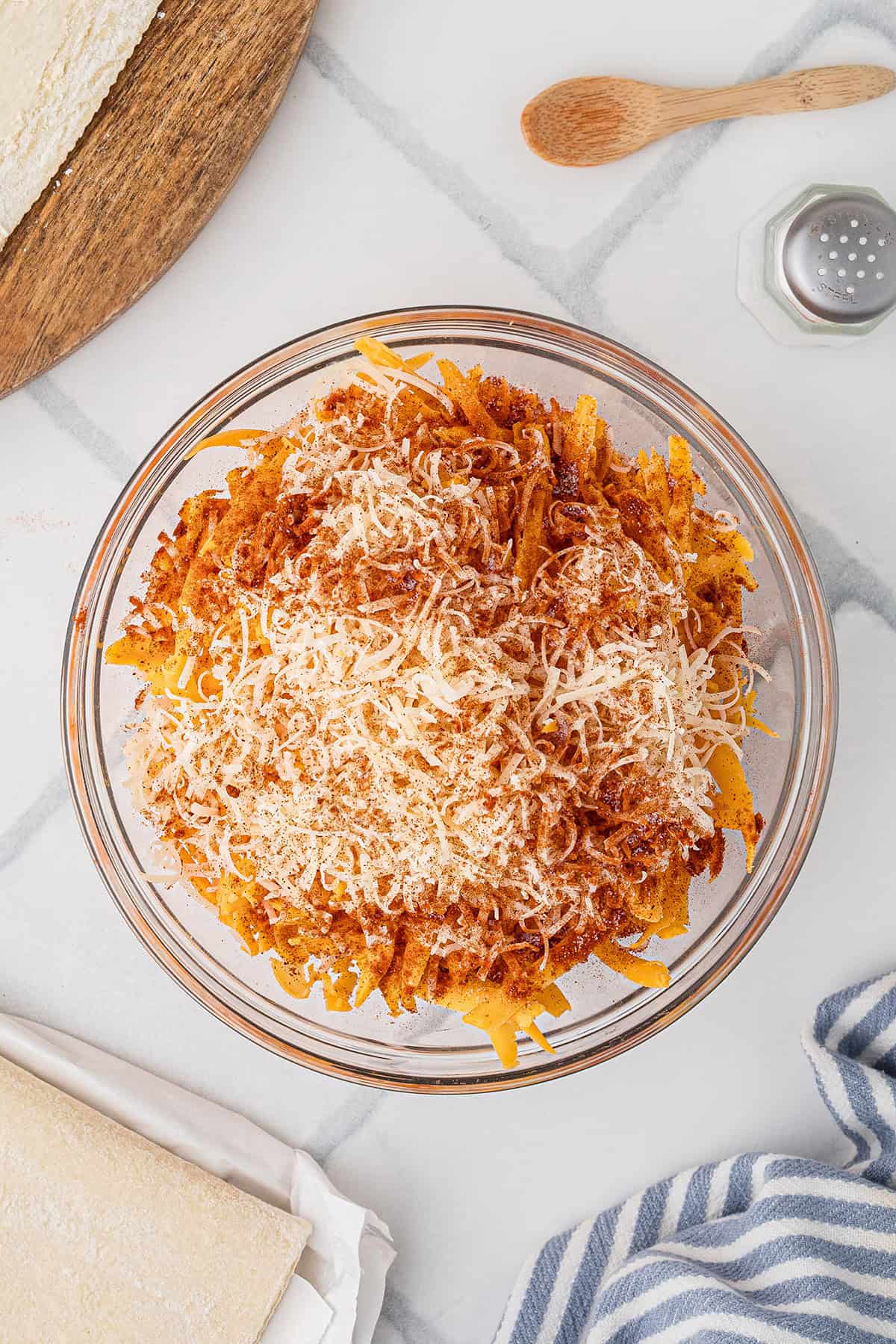 A glass bowl filled with grated cheese and seasonings on a white countertop.