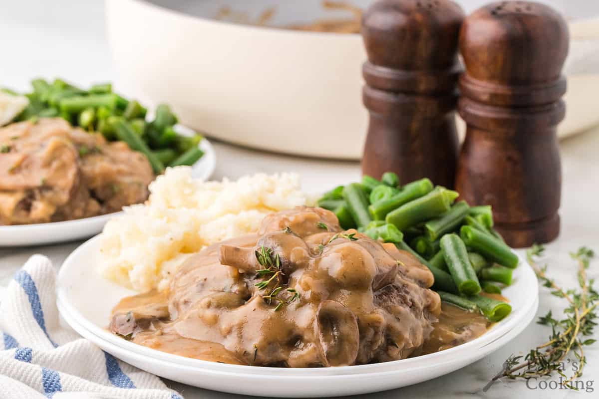 Plate with Salisbury steak in brown gravy, mashed potatoes, and green beans; salt and pepper shakers in background.