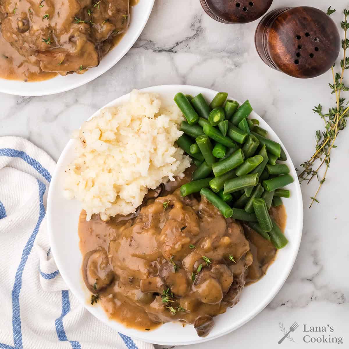 A plate with mashed potatoes, green beans, and Salisbury steak with brown gravy, next to salt and pepper shakers.