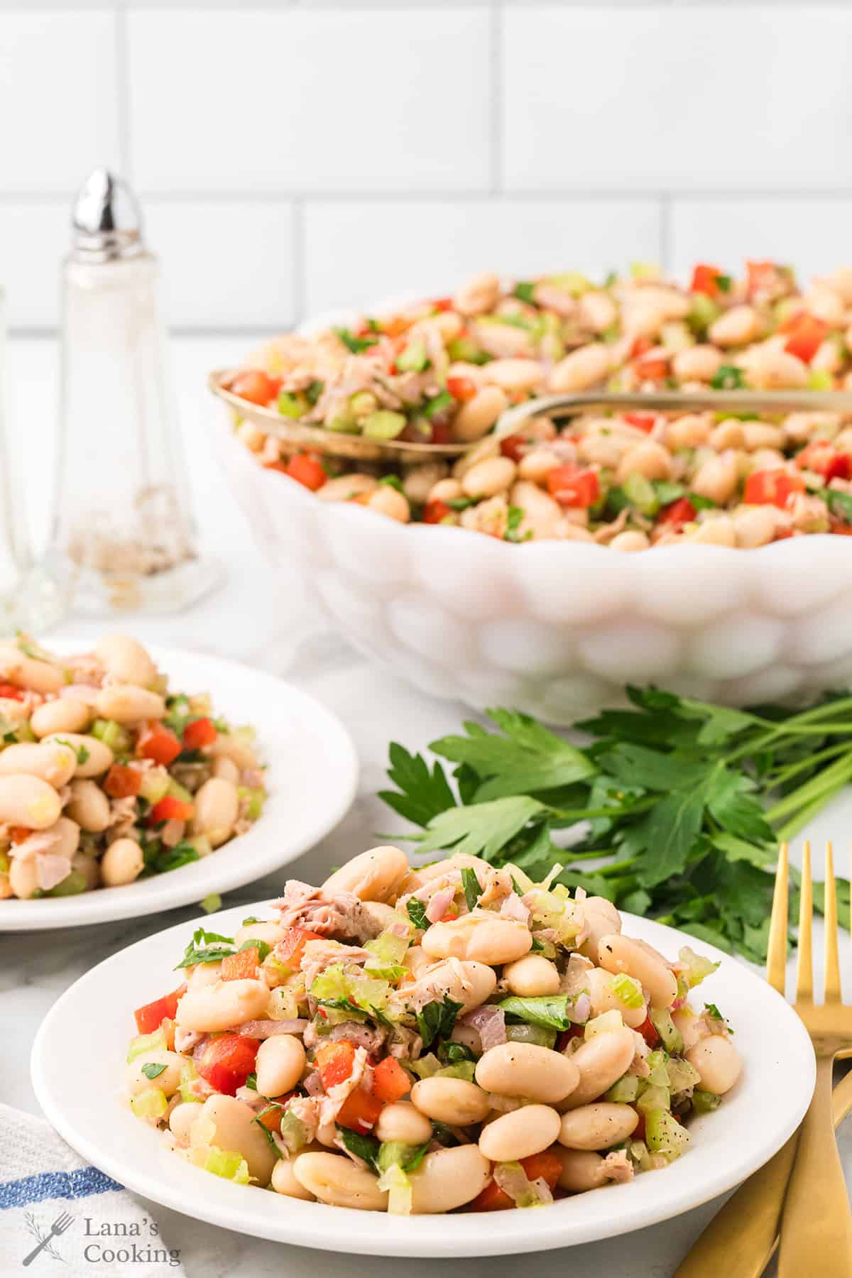 A plate and bowl of white bean tuna salad with chopped vegetables, garnished with fresh parsley on a table.