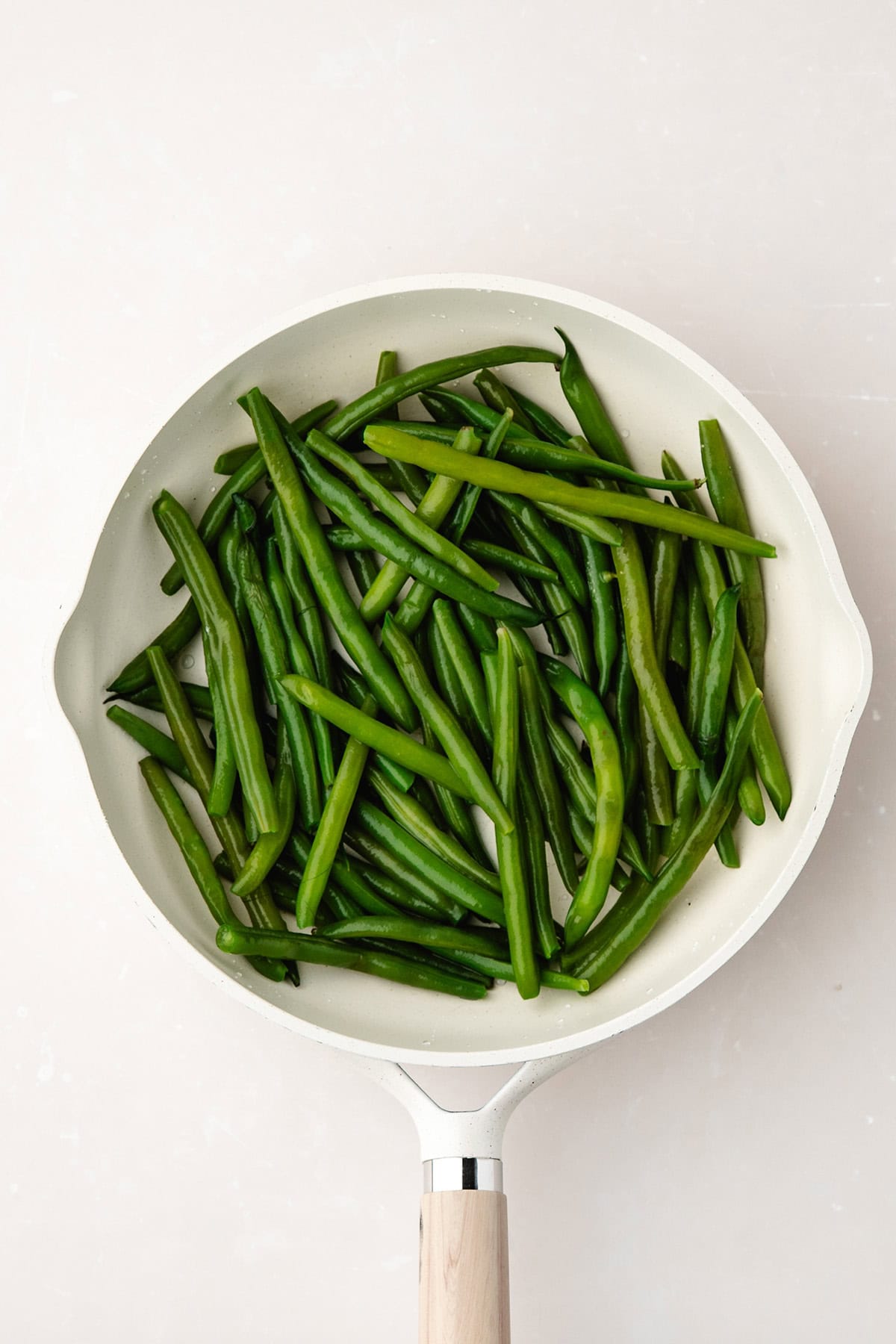 A white pan filled with fresh green beans on a light-colored surface.