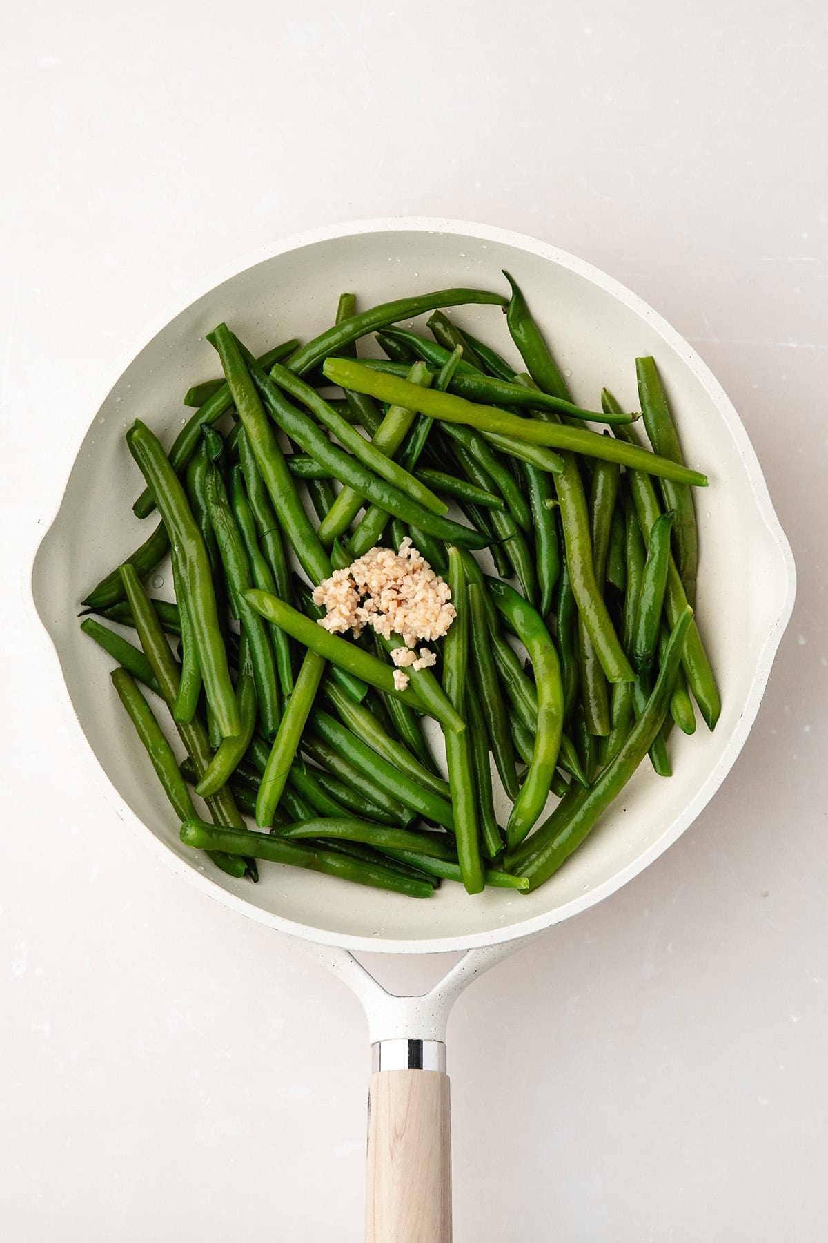 A white skillet with cooked green beans and a mound of minced garlic in the center.