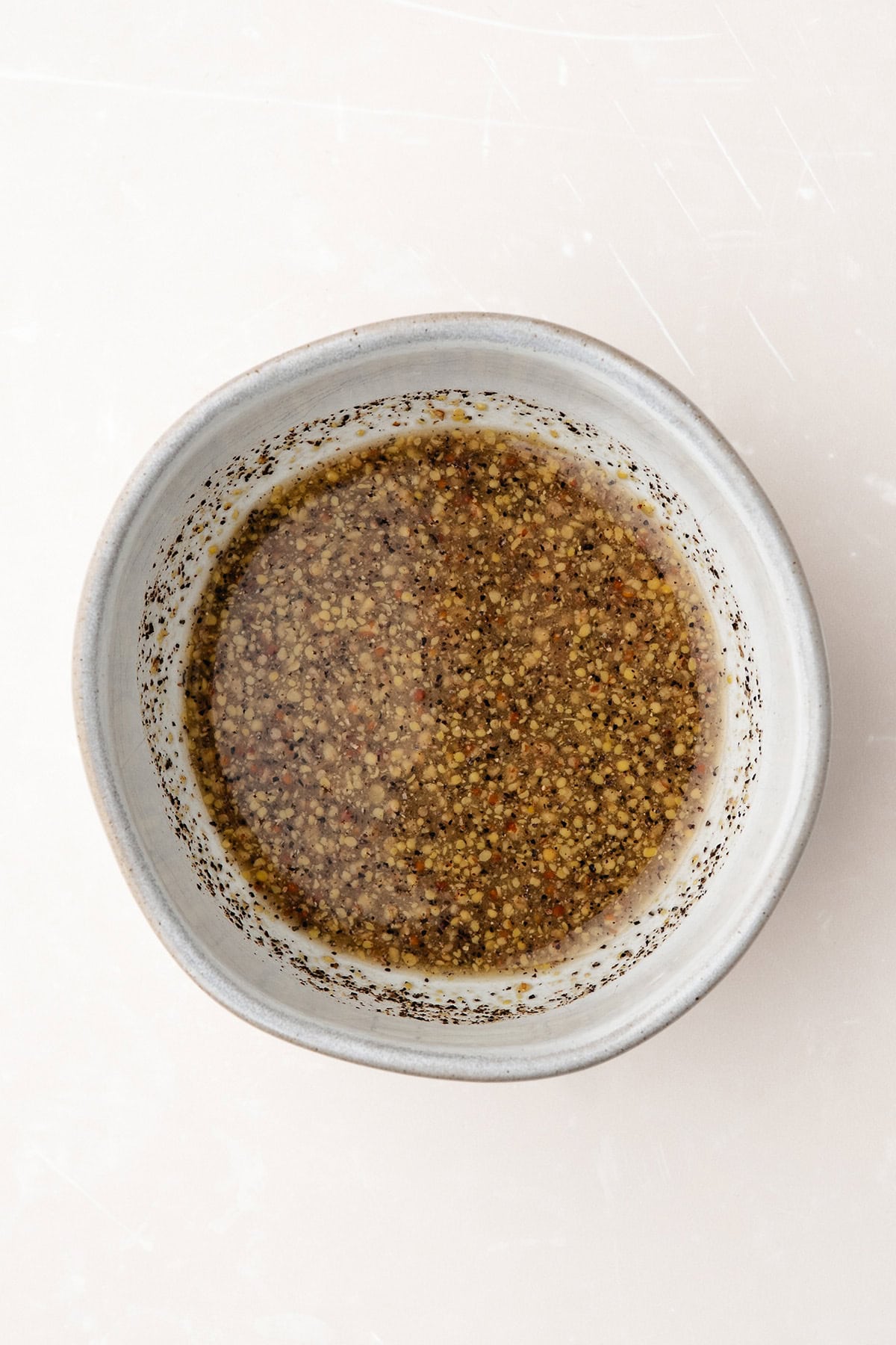 Small ceramic bowl filled with a coarse, brownish mustard vinaigrette on a light surface.