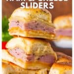 Stacked ham and cheese sliders on golden buns, with melted cheese and poppy seeds on top, on a plate.