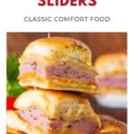Two ham and cheese sliders stacked on a plate with melted cheese and golden buns.