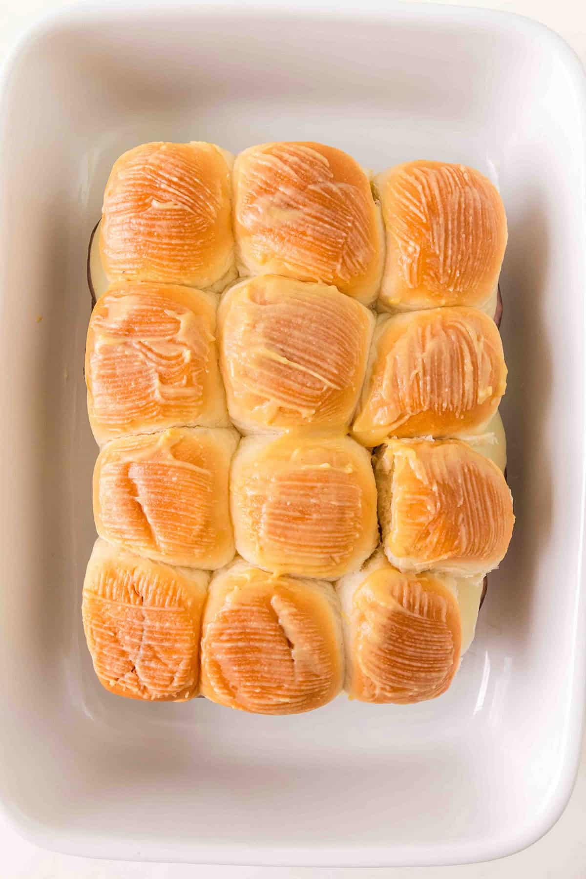 Twelve golden brown sliders arranged neatly in a white baking dish.
