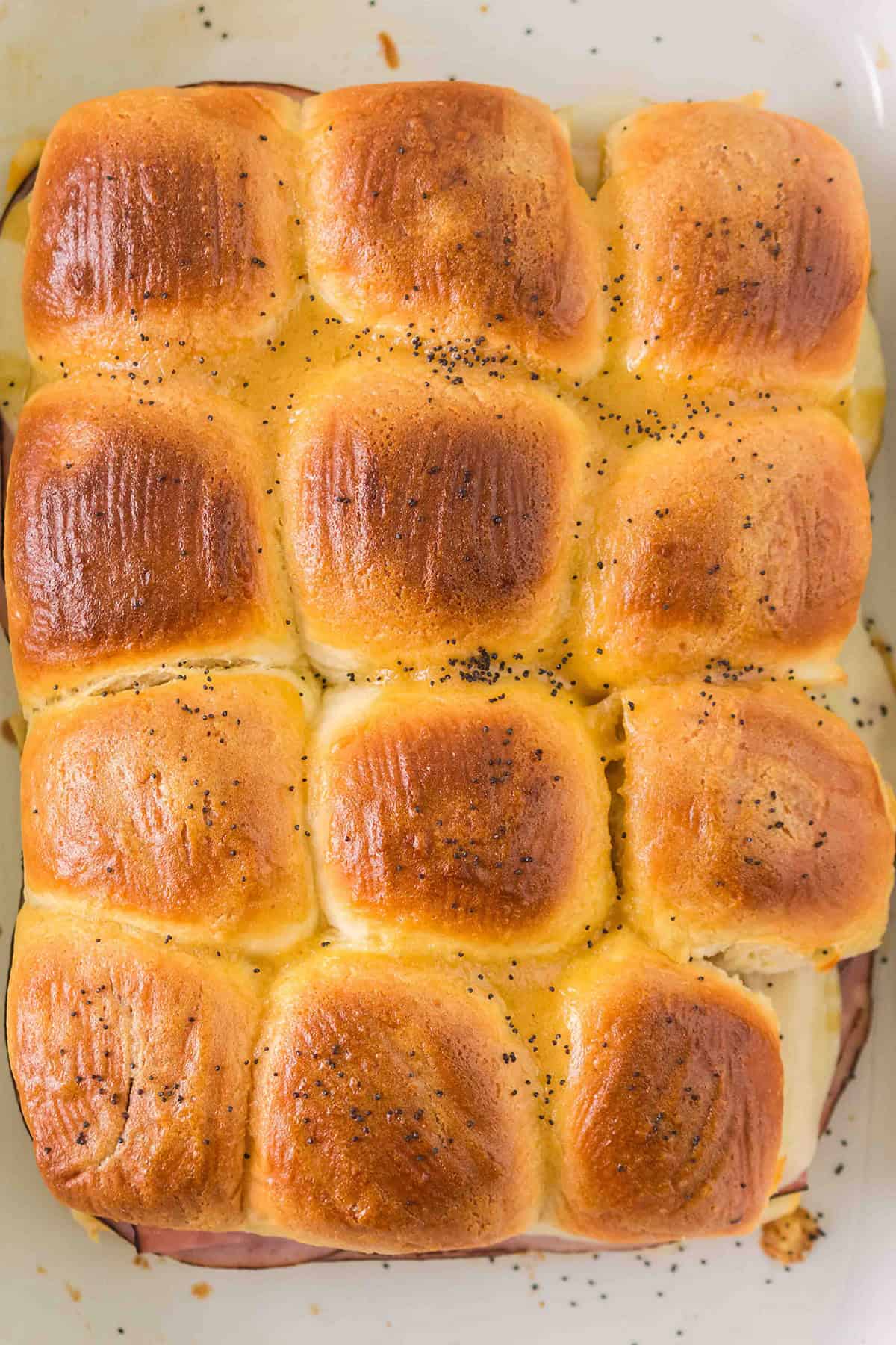 Nine golden-brown sandwich sliders baked closely together, with melted cheese and poppy seeds on top.
